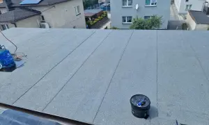 Nowy dach z papy na styropianie, gotowy na ochronę domu. Widać butlę gazową i wiadro z materiałami.