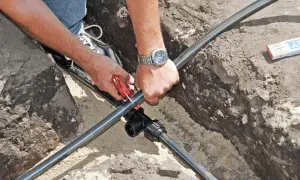 Hände schneiden Kunststoffrohr für die wasserleitung verlegen. Ein T-Stück wird vorbereitet.
