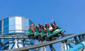 Ludzie na kolejce górskiej wesoło machają rękami. Dzięki **fastpass** uniknęli długiego czekania na tę ekscytującą przejażdżkę.