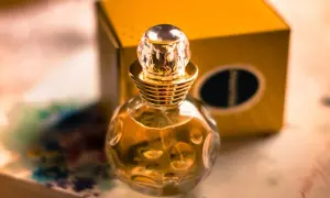 Złota buteleczka perfum Christian Dior Dolce Vita z kryształowym korkiem, obok żółtego pudełka.