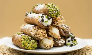 Stos idealnie udekorowanych cannoli z ricottą, posypanych cukrem pudrem, pistacjami i orzechami.