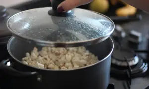 Ręka podnosi pokrywkę garnka, spod której widać gotowy popcorn. Tak właśnie robi się popcorn w garnku!