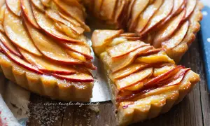 Una deliziosa crostata di mele, con fette di mela lucide disposte a spirale su una base dorata. Una fetta è stata tolta, rivelando la morbidezza.