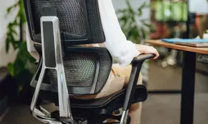 Person in bequemer Sitzposition am Schreibtisch, die Armlehne des Bürostuhls nutzend.