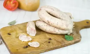 Swojska kiełbasa na desce, idealna na przepis 5 kg. Widoczne plastry, pieprz i liść laurowy.