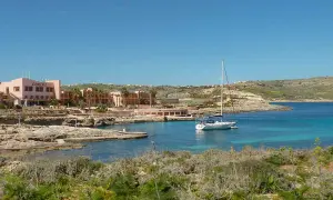 Traumhafter Urlaub auf Malta: Ein Segelboot ankert in einer Bucht vor dem Comino Hotel, umgeben von Felsen und mediterraner Vegetation.
