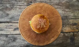 Hamburger z sezamem na drewnianej desce, widok z góry.