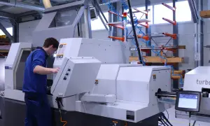 Młody pracownik obsługuje nowoczesną tokarkę CNC. Precyzyjna praca na tokarce wymaga skupienia i umiejętności.