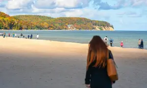 Jesień nad morzem. Spacerowicze na plaży, w oddali widać klify i las. Gdańsk Sopot odległość plażą.