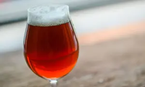 Un bicchiere di irish red ale con schiuma bianca, su un tavolo di legno.