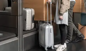 Osoby z bagażem podręcznym Austrian Airlines czekają w kolejce. Srebrne walizki gotowe do podróży.