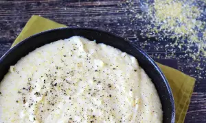 Krämig italiensk polenta i en gjutjärnspanna, strödd med svartpeppar. Majsgryn syns på den mörka träytan.