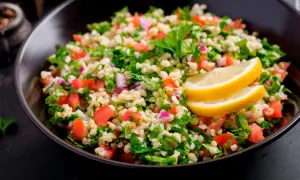 Delicioso tabule receta, una ensalada fresca de bulgur, tomate, perejil y cebolla morada, adornada con rodajas de limón.