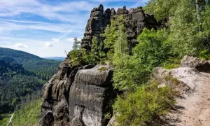 Felsformationen im Elbsandsteingebirge, ideal zum schmilka wandern. Ein Pfad führt durch üppige Vegetation zu den bizarren Felsen.