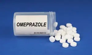 Białe tabletki z napisem OMEPRAZOLE rozsypane z pojemnika. Bioprazol pomaga w leczeniu dolegliwości żołądkowych.