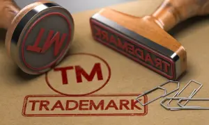 Dwa stemple z napisem "TRADEMARK" i symbolem "TM" na brązowym tle, obok spinaczy.