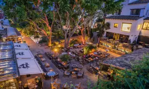 Wieczorny widok na tętniący życiem ogród restauracyjny z oświetlonymi drzewami i łukowym mostem w tle, przypominającym puente romano w Marbelli.