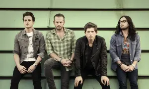 Czterech członków zespołu Kings of Leon siedzi na tle zielonej ściany.