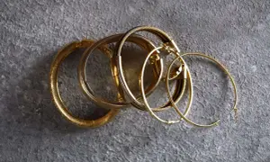 Un grupo de pulseras y aros dorados sobre fondo gris. Aunque el oro no se oxida, estas piezas lucen un brillo que evoca el paso del tiempo.