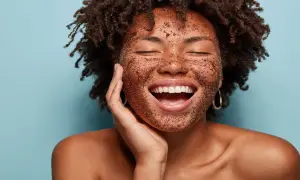Mujer sonríe con la cara cubierta de exfoliante, mostrando cómo exfoliar la piel para un brillo radiante.