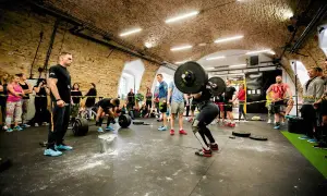 Kobieta podnosi sztangę w siłowni CrossFit, podczas gdy widzowie obserwują.