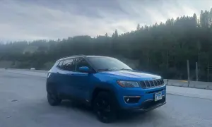 Blå Jeep Compass står vid vägkanten med en skog i bakgrunden. Kanske ett oväntat stopp, en Jeep Compass problem?