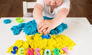 Dziecko bawi się masą sensoryczną i kolorowymi literami tworzącymi napis "SENSORY".