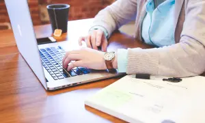 Kobieta pracuje na laptopie, obok notatnik i kubek z herbatą. Czyżby przygotowywała dokumenty dotyczące redukcji etatu i umowy na czas nieokreślony?