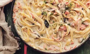 Tagliatelle w kremowym sosie z kawałkami łososia i ziołami w czerwonej patelni.