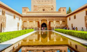 El Patio de los Leones en la Alhambra, con su estanque reflejando la arquitectura y un grupo de visitantes admirando la belleza.