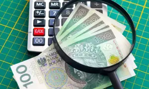 Kalkulator, lupa i polskie banknoty 100 zł na zielonym tle.