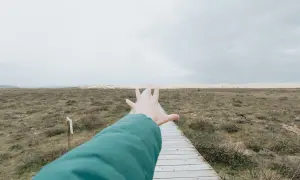 Ręka wyciągnięta w kierunku ścieżki, tworząc wrażenie **widzenia tunelowego** na tle krajobrazu.