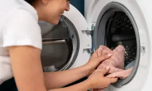 Donna sorride mentre mette un asciugamano rosa nella lavatrice, pronta per un bucato fresco.
