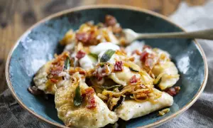 Pyszne pierogi z serem, okraszone skwarkami i cebulką, podane w niebieskiej misce.