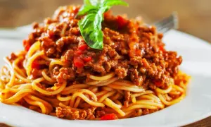 Porcja spaghetti bolognese z mięsem mielonym, sosem pomidorowym i bazylią na białym talerzu.