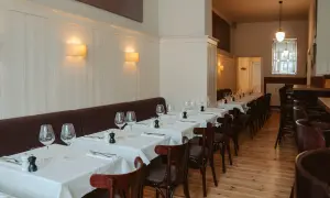 Elegantes Restaurant in Berlin, bereit für Gäste. Tische sind mit weißen Tischdecken, Gläsern und Besteck gedeckt. Gemütliche Atmosphäre dank Wandlampen.