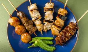 Różnorodne yakitori na niebieskim talerzu: kurczak, wątróbka, kulki mięsne i papryczki shishito.