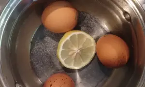 Cztery jajka i plasterek cytryny w garnku z wodą, gotowe do tego, jak ugotować jajko na twardo.