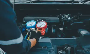 Tecnico con guanti controlla i manometri per ricaricare aria condizionata auto.
