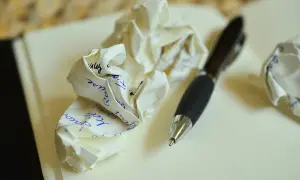 Zgniecione kartki z tekstem, być może próby napisania zaproszenia na ślub. Długopis obok sugeruje proces twórczy.