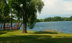 Malownicze jezioro Zelwa otoczone zielenią, z drewnianymi altankami przy brzegu.