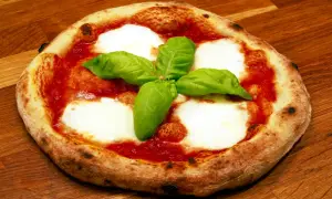 En napolitansk pizzadeg snabb, toppad med tomatsås, mozzarella och färsk basilika, ligger på en träyta.