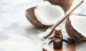 A small bottle of coconut oil sits near a halved coconut and a wooden spoon with coconut flakes. This image prompts the question: is coconut oil safe for cats?