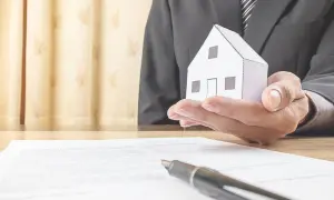 Un uomo in giacca e cravatta tiene una casetta di carta, simbolo di un accordo di leasing immobiliare per privati.