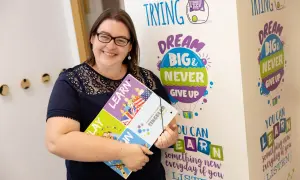 Mujer sonríe, sosteniendo un portafolio con la palabra "LEARN". El fondo tiene frases motivacionales sobre aprender, como "DREAM BIG & NEVER GIVE UP". El primer nivel de inglés es B1 o B2.