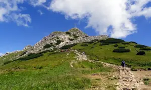 Kamienna ścieżka prowadzi na zielony zbocze, gdzie widać grupę turystów zmierzających na Giewont szczyt.
