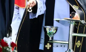 Osoba w szatach liturgicznych sypie ziarna. Czy to apostata, kto to? Ceremonia z mikrofonem i kielichem.