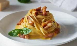 Spaghetti carbonara – przepis oryginalny ze śmietaną. Pyszne danie z makaronem, boczkiem i kremowym sosem jajeczno-serowym, udekorowane bazylią.