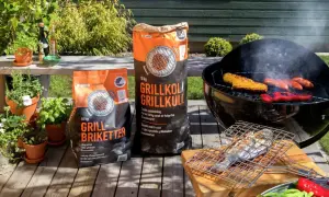 Två säckar med grillkol eller briketter står redo för grillkvällen. Majskolvar, korvar och paprika ryker på grillen.