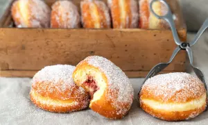 Frisch gebackene Berliner, mit Zucker bestreut, warten auf das perfekte Berliner Rezept. Eine Marmeladenfüllung ist sichtbar.